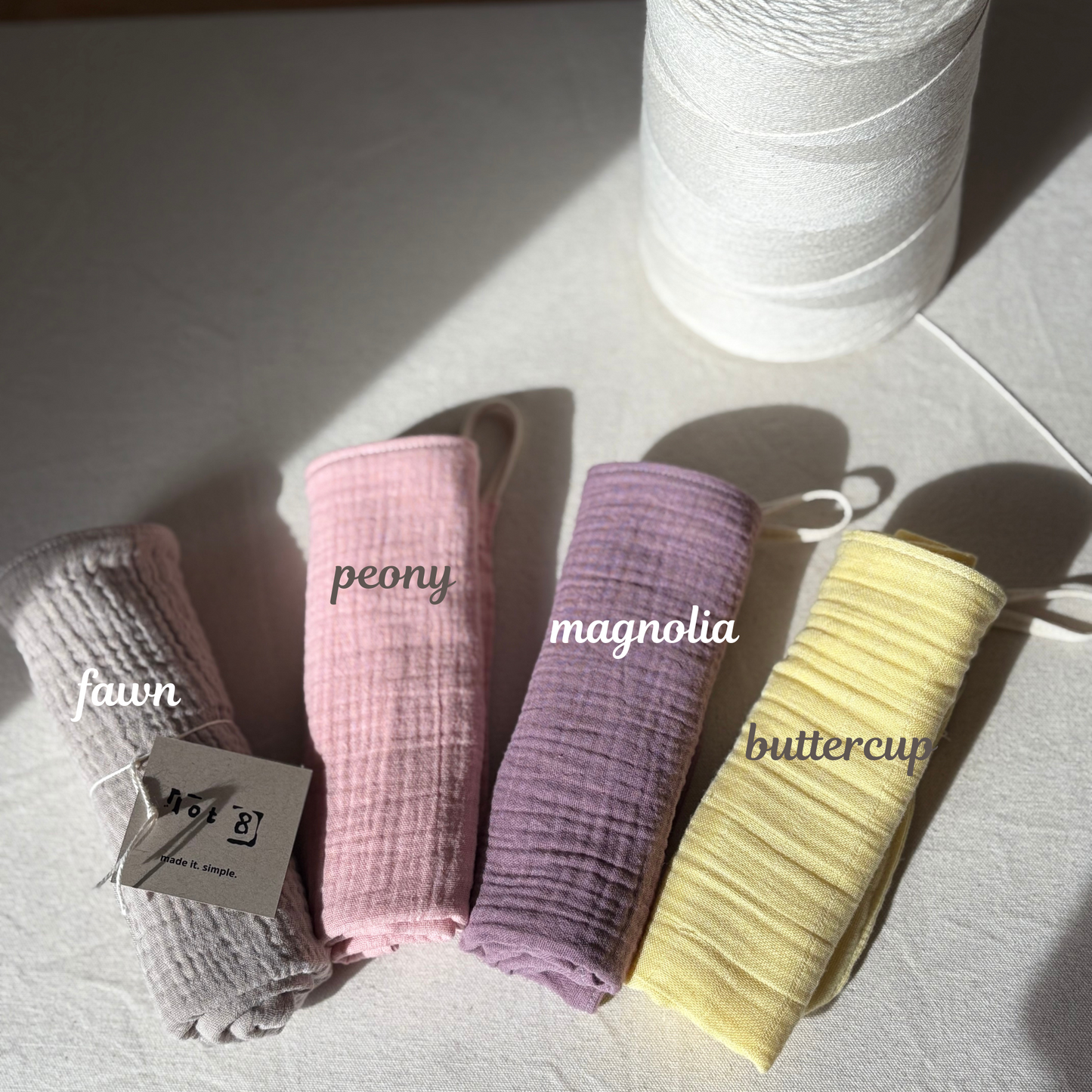 4 facial cleansing cloths are rolled up and laid alongside each other. Fawn is a light taupe. Peony is a soft pink. Magnolia is an earthy purple and Buttercup is a soft yellow.