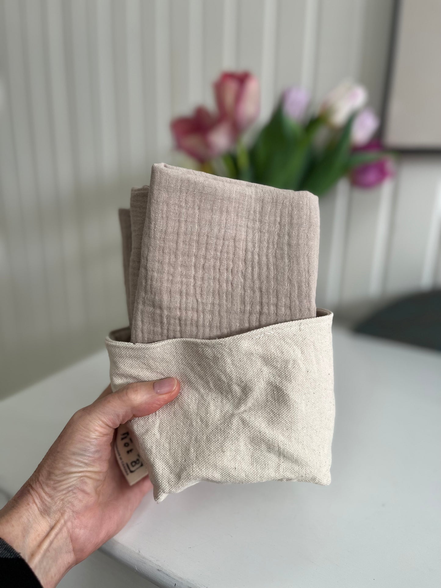 A hand holds the fabric bucket with 4 cleansing cloths inside.