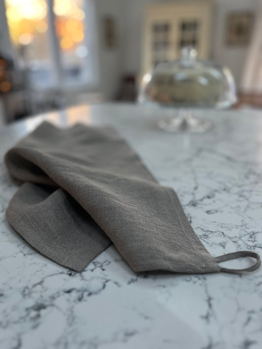 Natural tea towel laying on a granite surface. A glass cake stand in the background