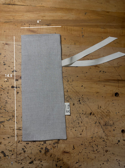 A natural-coloured linen wine sack with two cream ties, laid flat on a wooden surface. White measurement lines and text indicate dimensions of 6 inches by 14.