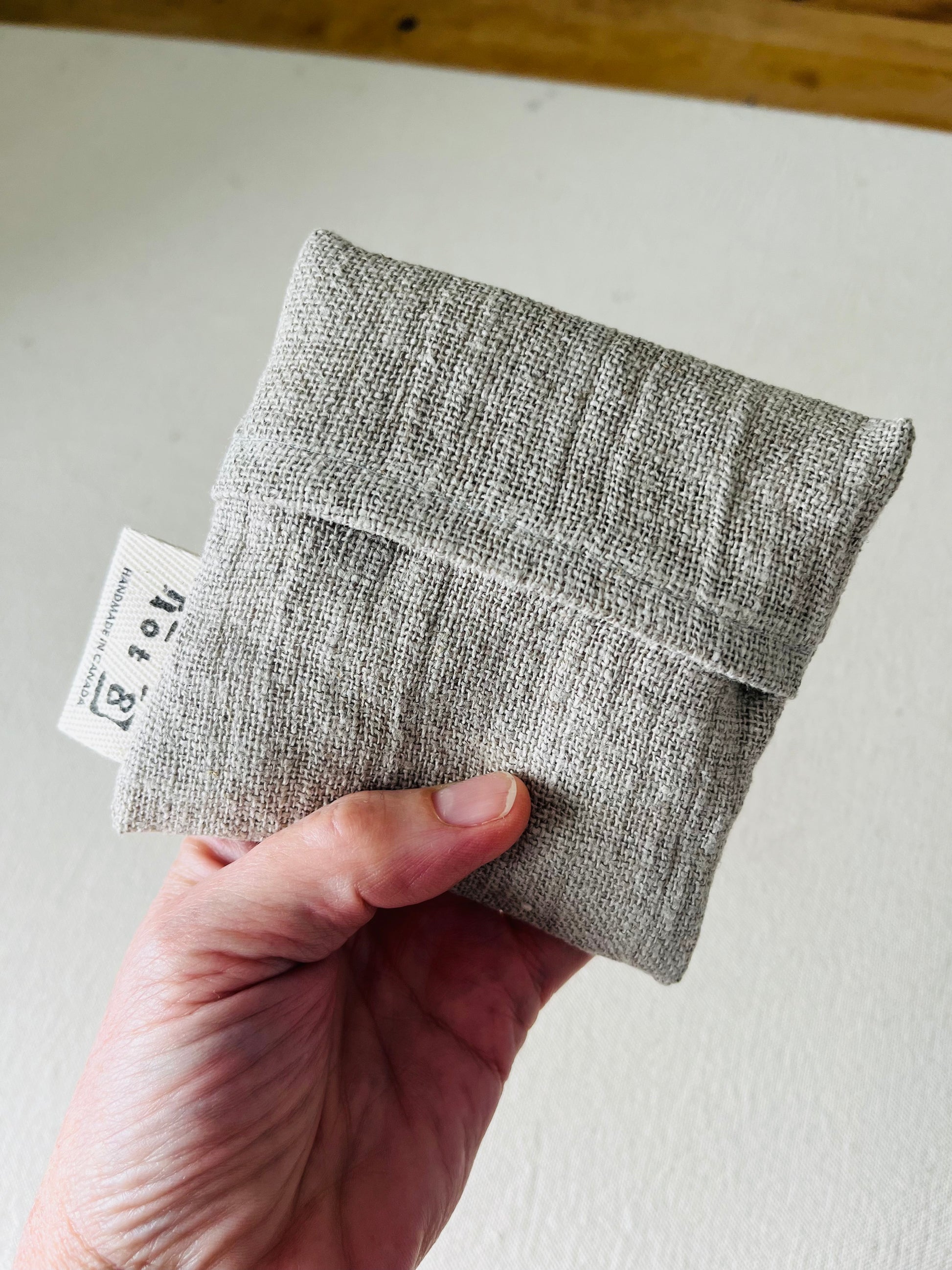 An adult hand holds up the Boo Boo Bag. The open weave of the natural linen and the cotton twill lot8 tag go hand in hand with this natural product.