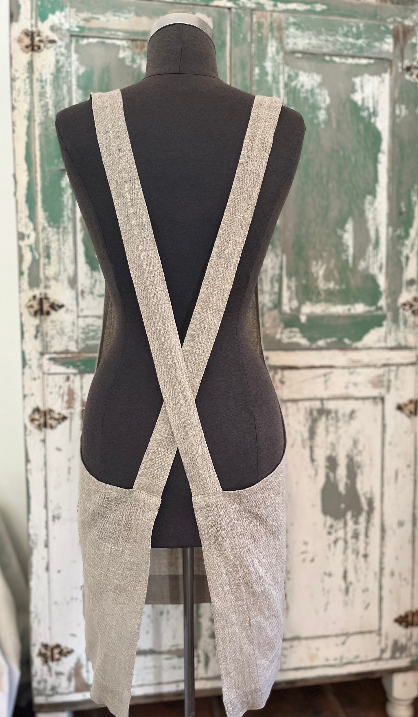 A dressmaker's Judy displays the back of the  linen crossback apron with two pockets. A vintage green and white cabinet stands in the background. 