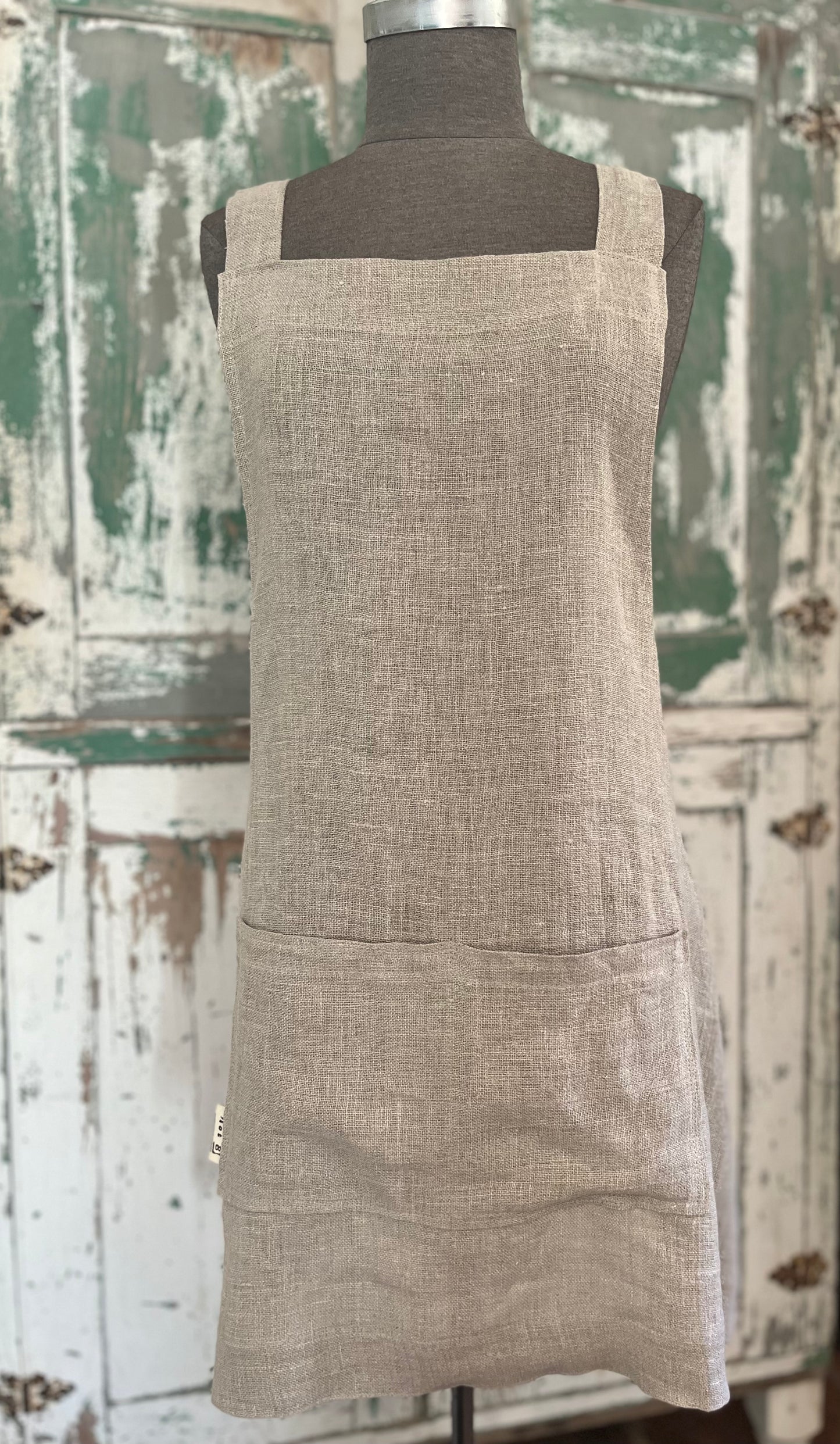 A dressmaker's Judy displays the linen crossback apron with two pockets. A vintage green and white cabinet stands in the background. 