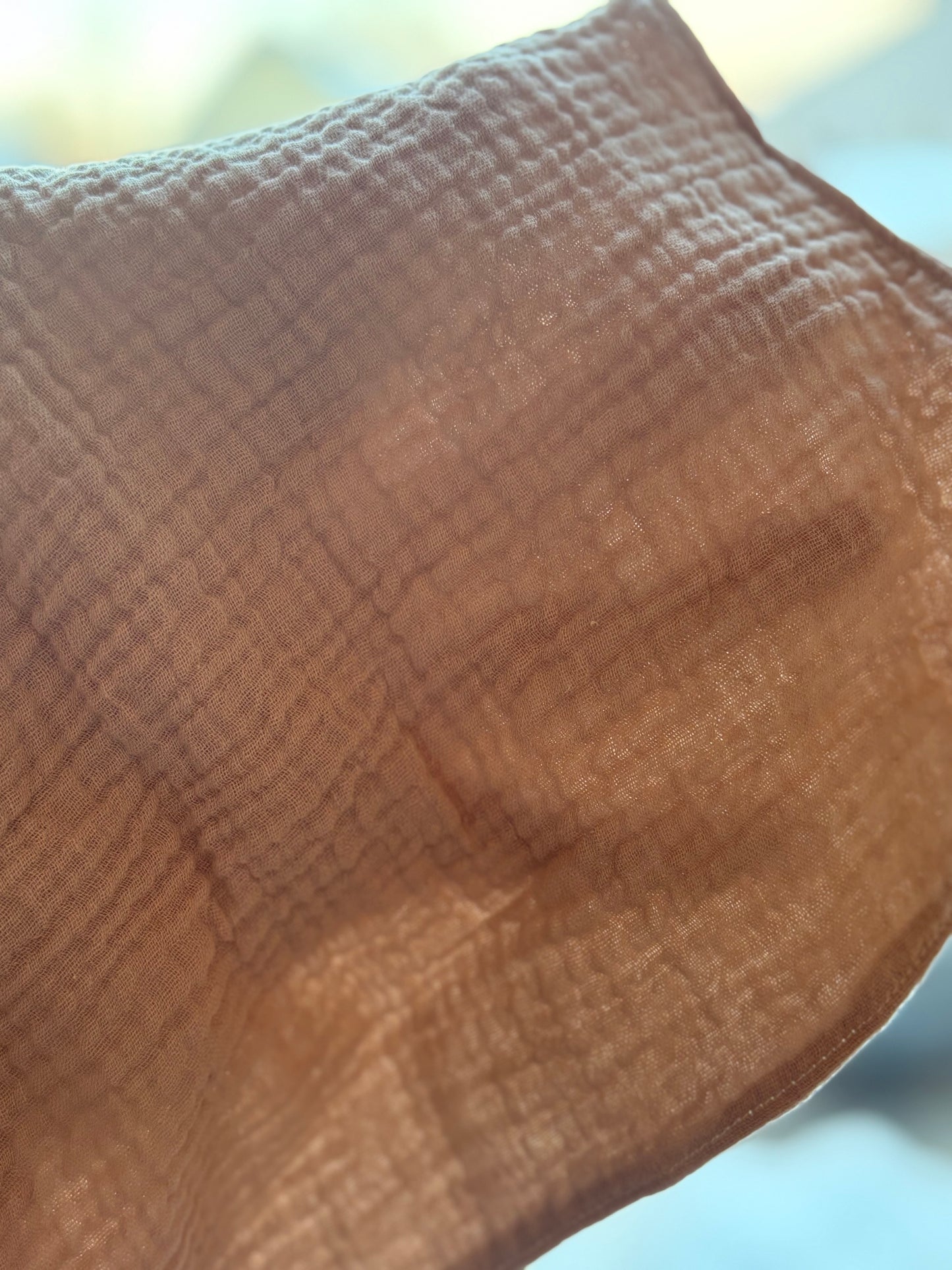 A close-up of a textured, semi-sheer light fawn-coloured cleansing cloth,with a fine grid-like weave pattern.