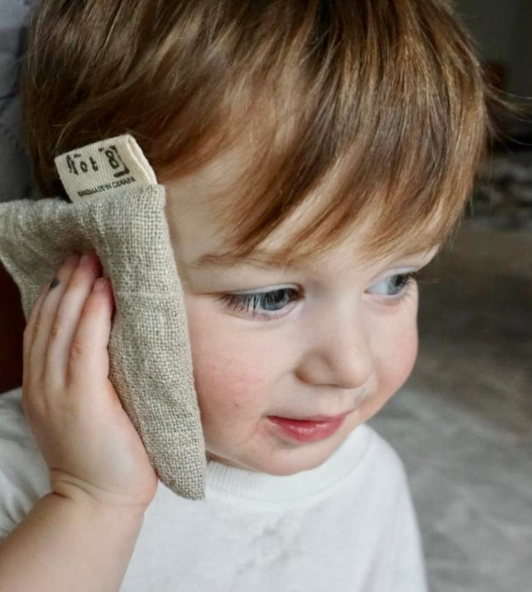 A toddler with tawny hair and  blue eyes holds the boo boo bag gently against his  head. 