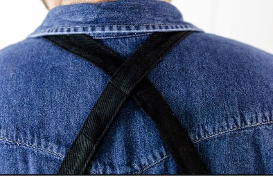 Close-up of the cross-back strap design and secure parachute clip closure on a black cotton chef apron.