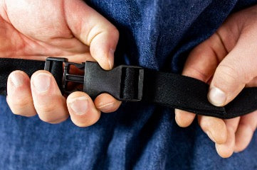 Close-up of the cross-back strap design and secure parachute clip closure on a black cotton chef apron.