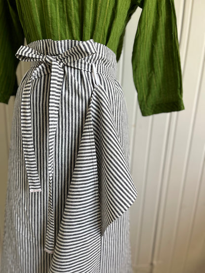 A close up of the black and white striped bistro apron on the dressmaker's Judy. The waist strap of the apron is threaded through the loop of a coordinating hand-towel .