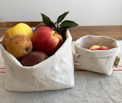 The large and small bucket sit on a table side by side. The large is filled with several pieces of fruit; the small holds a single apple