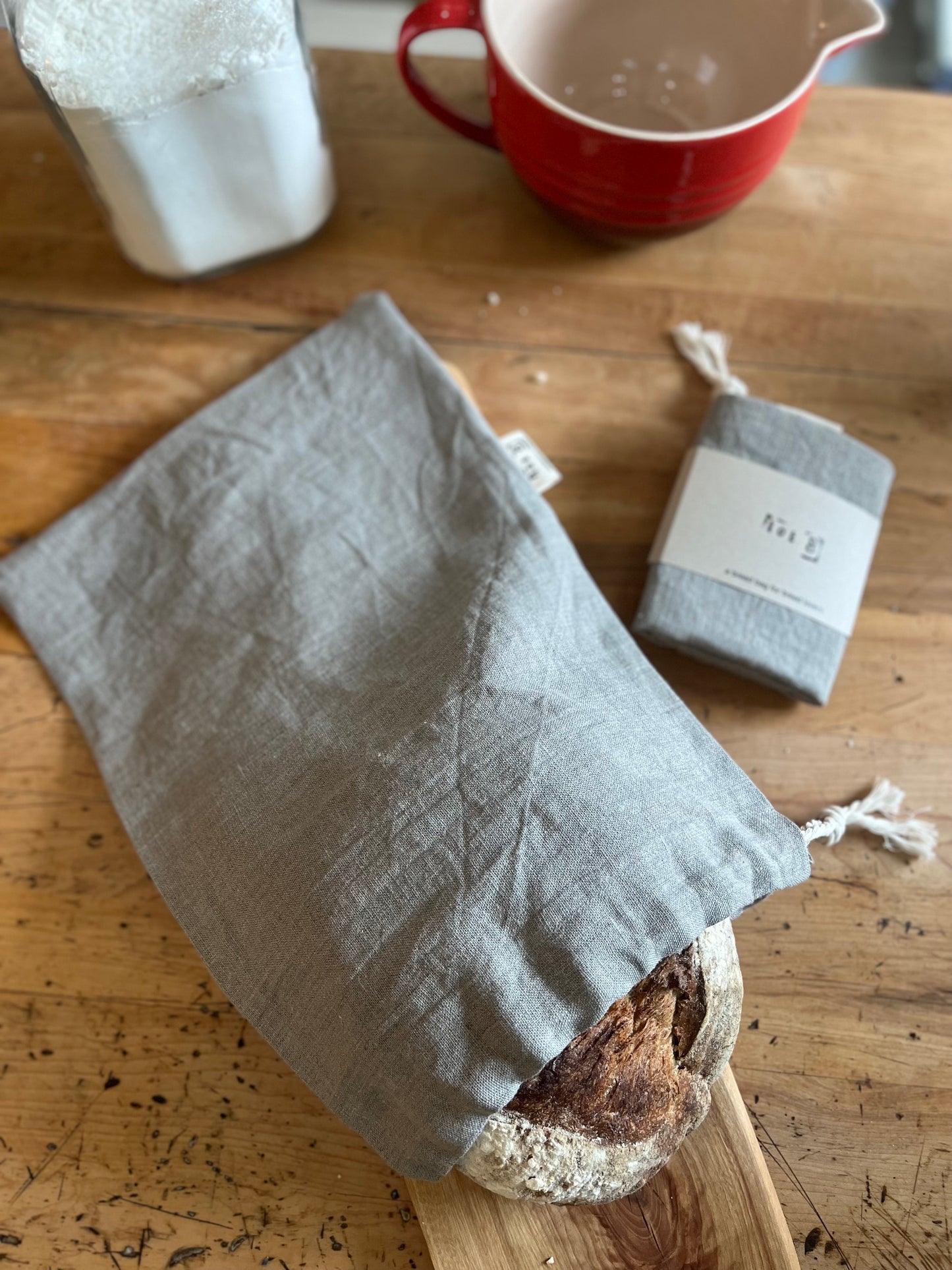 A handsewn linen bread bag with bread peaking out. Packaged bread bag  sits beside it.