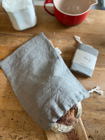 A handsewn linen bread bag with bread peaking out. Packaged bread bag  sits beside it.