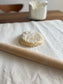 A small disc of dough sits on a pastry cloth. Rolling pin in the foreground; jar of flour in the background