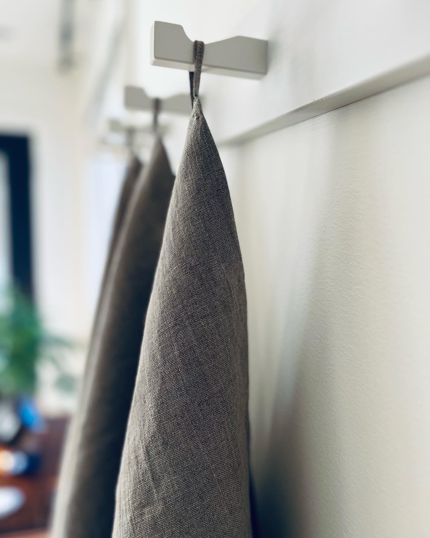 The tea towel hangs from its loop on a white wooden peg rail. A fern stands in the background.