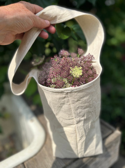 A hand holds the strop of the posy tote filled with flowers
