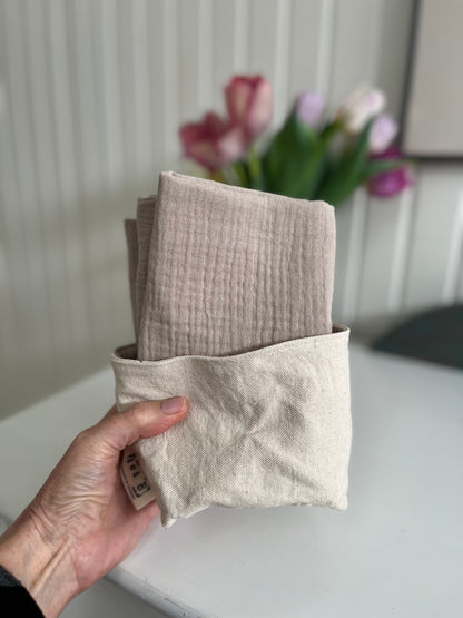 A hand holds the fabric bucket with 4 cleansing cloths inside.