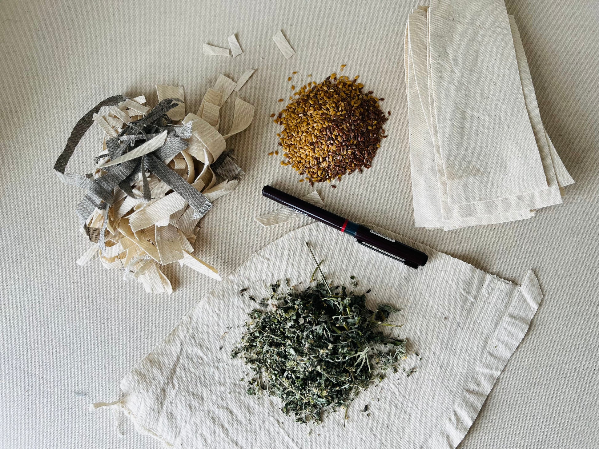 The components of the cat toy are shown: a small mound each of all-natural fabric scraps , flax seed, catnip and some strips of cotton canvas ready for sewing.