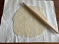 Pastry dough has been rolled out on a cotton canvas pastry cloth. A rolling pin lays across the butter studded dough.