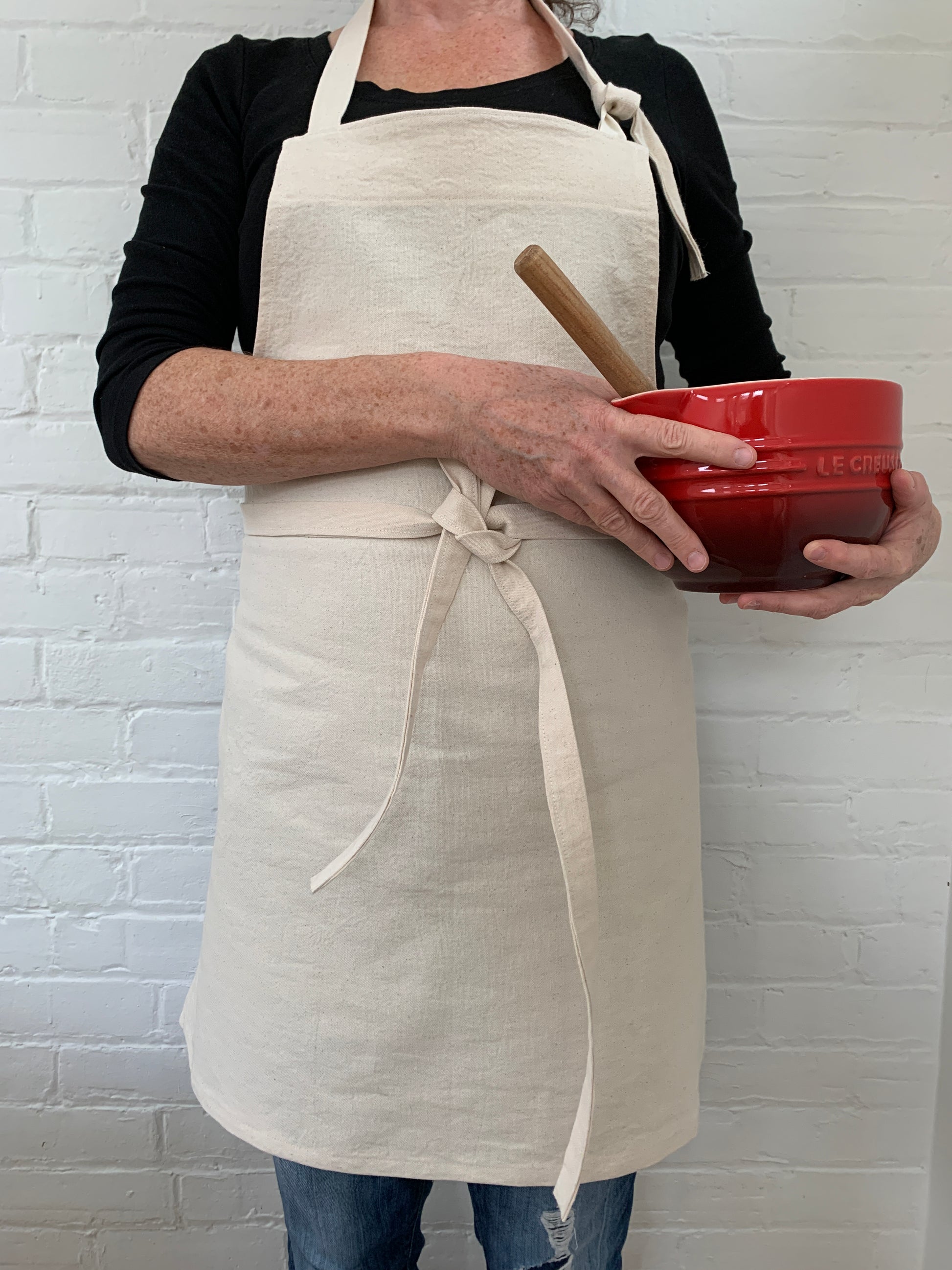 Woman wearing cotton canvas apron and holding red mixing bowl