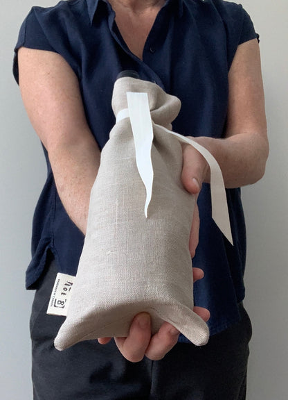 A woman offers a bottle of wine in a 100% linen reusable wine tote