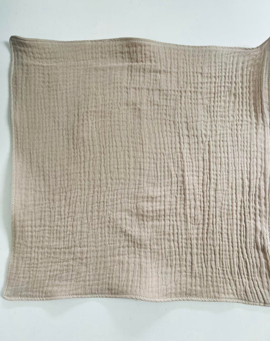 A close up of one face cloth on a white background. The texture of the double gauze cotton shows clearly. The edges of the cloth are sewn to prevent fraying. The colour is a light beige called fawn.