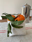 The small bucket filled with leafy clementines. A pot of coffee is in the background